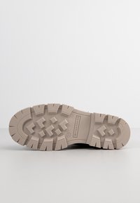 Semelle d'une chaussure beige robuste avec des crampons profonds, indiquée en taille 37 et marquée Tom Tailor, sur un fond blanc uni.