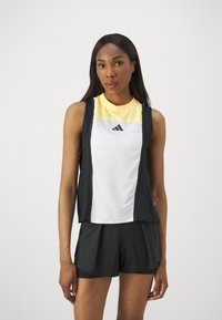 Schwarz-weißes Sport-Tanktop mit gelbem Kragen, runder Ausschnitt und Logo. Kombiniert mit schwarzen Shorts, glatte Textur.