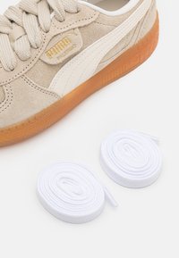 Baskets en daim beige avec des accents en cuir blanc et une semelle en gomme. Comprend deux lacets blancs. Présente le logo PUMA en or.