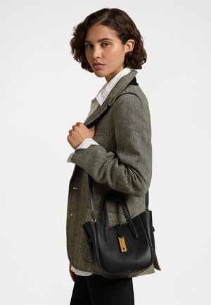 Sort læder håndtaske med struktureret overflade, guldfarvet hardware og korte håndtag. Modellen bærer en herringbone-jakke over en hvid skjorte.