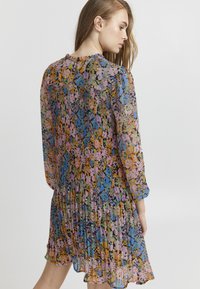 Ziedu kleita ar garām piedurknēm, izgatavota no viegla auduma. Daudzkrāsains raksts ietver zilo, rozā un dzelteno krāsu; plecu dizains aizmugurē.