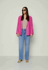 Φωτεινός ροζ σακάκι σε δομή πάνω από ένα ριγέ τοπ, σε συνδυασμό με απλές τζιν σε ανοιχτό μπλε και πράσινες σαγιονάρες. Μαύρα γυαλιά ηλίου ολοκληρώνουν την εμφάνιση.