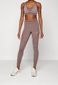 Zestaw sportowy w stonowanym mauve, składający się z crop topu z dekoltem w serek i paskami, połączony z legginsami o wysokim stanie i lekkimi sneakersami.