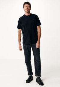 Černé bavlněné tričko s krátkým rukávem a malou nášivkou na hrudi, kombinované s tmavými denimovými džínami a černými kotníkovými botami.