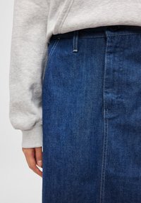 Saia de ganga em azul escuro com um design reto. Apresenta costuras visíveis e uma cinta, combinada com um sweatshirt cinzento.