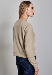 Beige tröja med rund halsringning och långa ärmar, med en figurnära midja och en slät textur. Parat med mörkblå denimjeans.