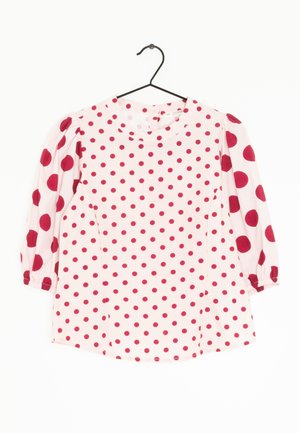 Röd blus med prickar, rund hals och ärmar i tre fjärdedelar. Tillverkad av lättviktsmaterial, har detaljer med samlade ärmslutar och sidoseams.