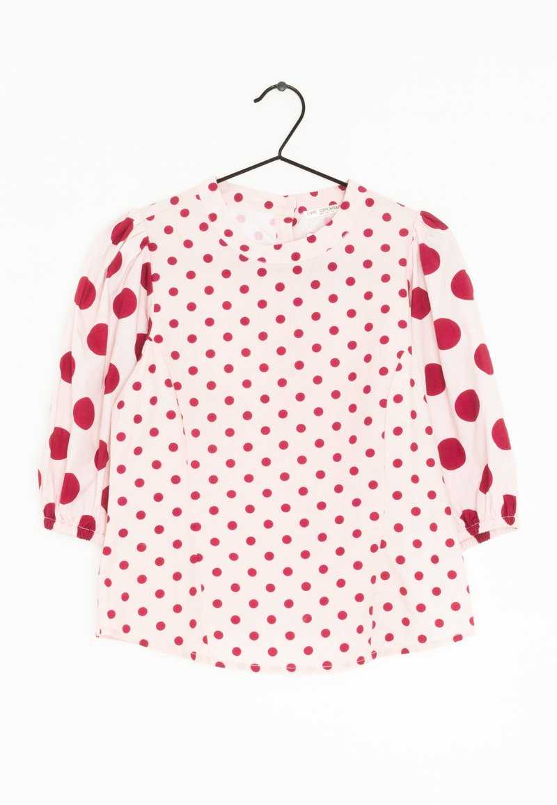 Blusa rossa a pois con collo rotondo e maniche a tre quarti. Realizzata in tessuto leggero, presenta polsini delle maniche arricciati e cuciture laterali.