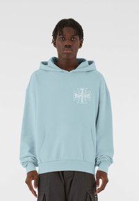 Svetlomodrá mikina s kapucňou vyrobená z mäkkého materiálu, s prednou vreckom a potlačenou grafikou na ľavej strane hrude. Uvoľnený strih a rebrované manžety.