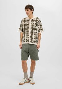 Kortærmet beige og olivenmønstret polo-shirt sat sammen med olivenfarvede shorts, cremefarvede og grønne sneakers samt lysegrå sokker.