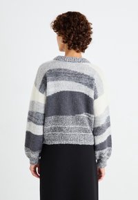 Pull rayé gris et blanc avec un col rond et des poignets côtelés. Le design présente une texture et une épaisseur variables sur l'ensemble du tissu.