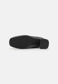 Suela de zapato negra con una superficie texturada, forma rectangular y un tacón de bloque modesto. El material parece duradero con un ligero brillo.
