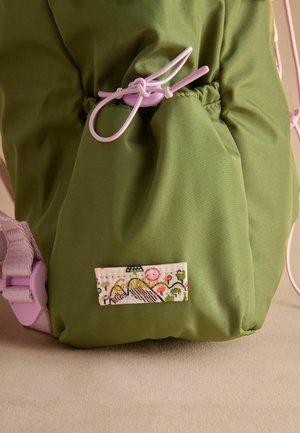 Green nylon bag featuring a drawstring closure, light pink cords, and a decorative label with a floral design and mountain pattern.