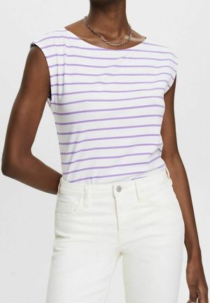 Person iført hvide bukser og en hvid ærmeløs top med lyse lilla vandrette striber og en simpel kædehalskæde.