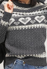 Harmaa neulepusero, jossa valkoisia sydänkuvioita ja geometrisia kuvioita. Paksu resorinen pyöreä kaulus ja helma, alareunassa pieni bränditunniste.