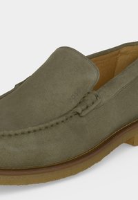 Mocassin vert en daim à enfiler avec couture mocassin et semelle en caoutchouc brun clair, vue partielle latérale et de dessus.