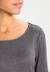 Gray long-sleeve shirt made of soft, textured fabric featuring a wide neckline and smooth finish, emphasizing comfort and simplicity.
