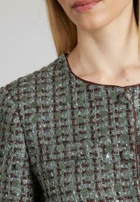 Strukturierte grüne und braune Tweed-Jacke mit Rundhalsausschnitt, Knopfverschluss und dekorativen Pailletten, die im Stoff eingebettet sind.