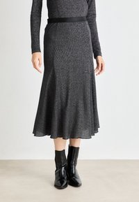 Black midi skirt with a flared silhouette, made of a sparkly, textured fabric. Features a smooth waistband and is paired with black ankle boots.