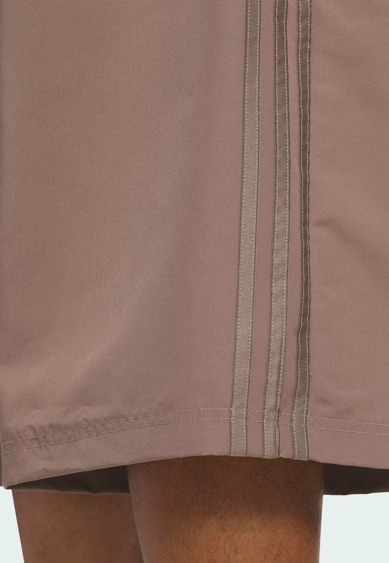 Close-up of beige fabric with three vertical stitched stripes alongside a person's leg visible below the hemline.