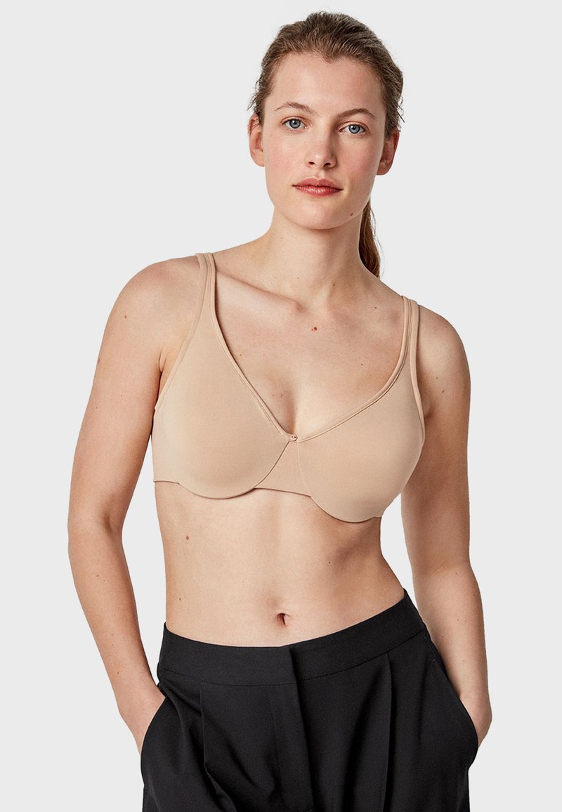 Soutien-gorge beige sans couture avec un décolleté plongeant, des bretelles larges et une fermeture à crochets. Tissu lisse avec un léger éclat et des détails de couture minimaux.