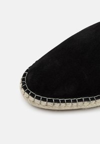 Espadrille en suède noir avec un bout rond, dotée d'une semelle en jute tressé et d'une couture contrastante le long du bord.
