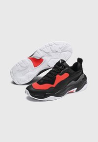 Czarno-czerwone sportowe sneakersy z teksturowaną cholewką, wyściełanym kołnierzem, grubą białą podeszwą środkową i wzorzystą podeszwą gumową.