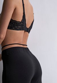 Soutien-gorge en dentelle noire avec des bretelles réglables et une fermeture à crochets ; associé à un legging noir sans couture avec une taille élastique haute.