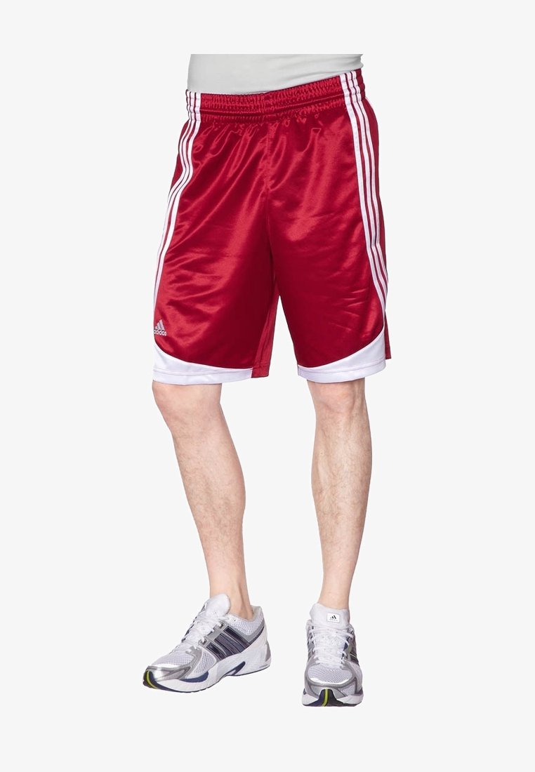 Homme portant un short de sport rouge et blanc Adidas et des chaussures de course blanches, se tenant devant un fond blanc.