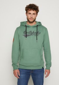 Grüne Baumwollkapuzenjacke mit Fronttasche, Kordelzugkapuze und einem auf der Brust aufgedruckten Logo. Verfügt über braune Ellbogenpatches und gerippte Bündchen.