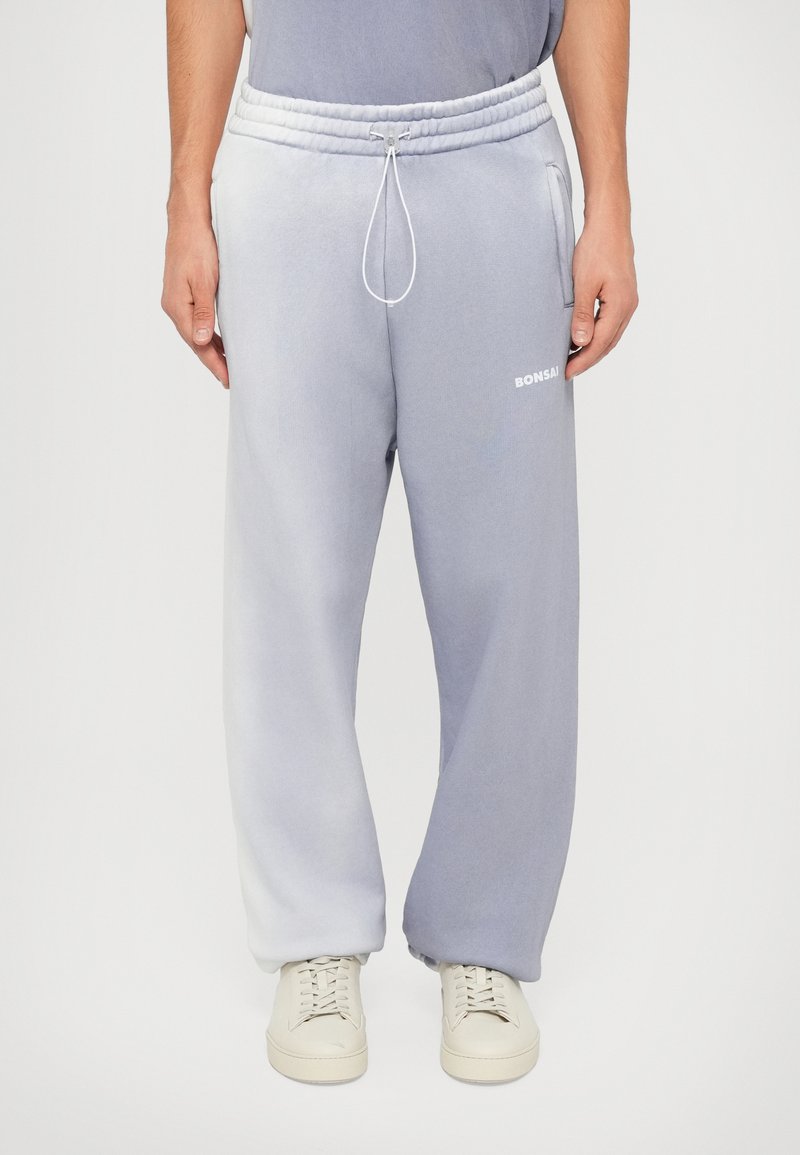 Pantaloni della tuta grigi ombre con vita regolabile tramite cordoncino, polsini elastici, tasche laterali e logo "BONSAI" in bianco sulla gamba sinistra.
