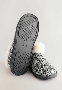 Black and white textured slippers with a soft white fur lining, rubber sole embossed with "RELAX," and a sleek shape for comfort.