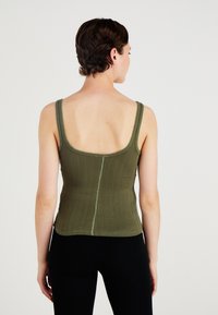 Ribbed, olive green tank top with a scoop back, featuring thin straps and a seam down the center. Fabric has a smooth texture.