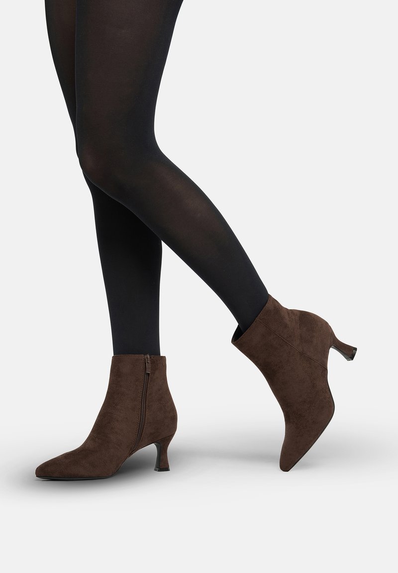 Botines de ante marrón con punta afilada, cierre con cremallera y tacón modesto, mostrados junto a medias negras.