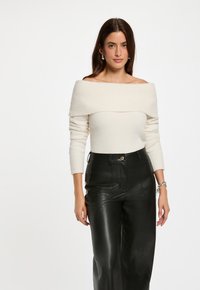 Maglione crema a spalle scoperte in maglia con tessuto testurizzato e maniche lunghe, abbinato a pantaloni neri in similpelle a vita alta con tasche anteriori.