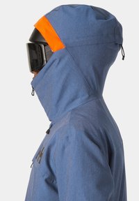 Giacca da sci blu con un accento arancione sul cappuccio, colletto alto, tasche con zip e vestibilità aerodinamica. Texture opaca; materiale resistente.