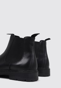 Botas Chelsea de cuero negro con paneles laterales elásticos, lengüetas para tirar y una suela de goma gruesa. Textura suave con detalles cosidos.
