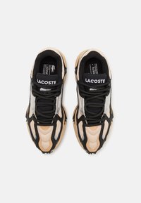 Sneaker Lacoste con tomaia in mesh beige e nera, con dettagli argentati, lacci neri e suola texturizzata per una migliore aderenza.