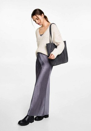 Pull crème en tricot avec un col en V, un débardeur gris, et une jupe noire à motifs violets foncés. Tenant un sac fourre-tout gris foncé, portant des bottines noires.