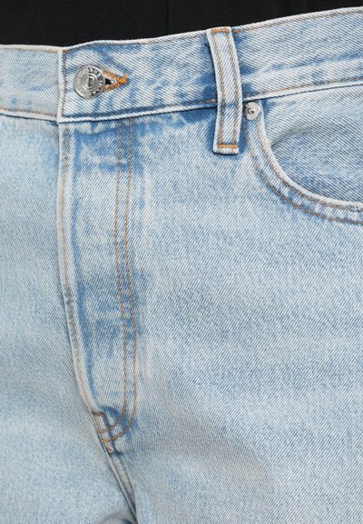 Világoskék farmernadrág, elhalványuló mintával, narancssárga varrással és ezüst gombbal a dereknál. Tartalmaz egy elülső zsebet.