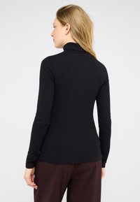 Czarny sweter z golfem o długich rękawach, prążkowanej fakturze, dopasowanym kroju i wysokim kołnierzu, zestawiony z ciemnymi bordowymi spodniami.