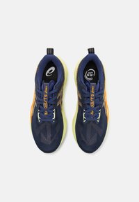 Zapatillas deportivas azul y amarillo con parte superior de malla texturizada, detalles en naranja, puntera redonda y suela acolchada. Los cordones son azul marino.