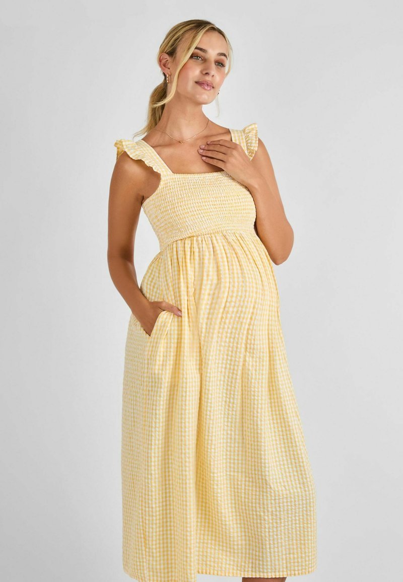 Vestido midi de cuadros amarillos con tirantes rizados, cuerpo elástico y bolsillos. Hecho de tela ligera, con un corte holgado.