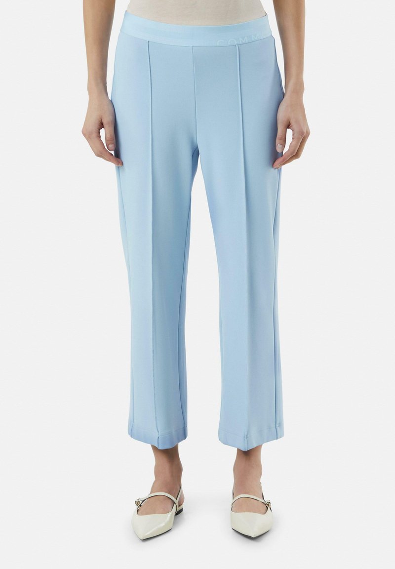 Lichtblauwe broek met een gladde textuur, met een brede tailleband en plooien aan de voorkant. De zoom is iets taps toelopend bij de enkels.