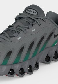 Baskets Nike Air Max grises et vertes avec tige en mesh texturé, semelle intermédiaire à motif avec coussinets noirs et laçage détaillé sur fond blanc.