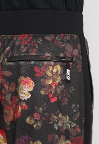Shorts de sport noirs à motif floral, dotés d'une texture en mesh, d'une taille élastique et d'une poche zippée avec une étiquette de marque.