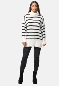 Pull en col roulé à rayures noir et blanc en tricot épais, avec une coupe ample et des poignets côtelés, associé à un jean noir ajusté et des bottines.