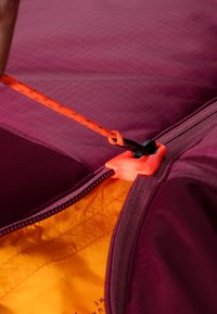 Giacca con zip di un profondo colore viola all'esterno, con un tirante arancione e un interno giallo a contrasto; texture liscia e design foderato.