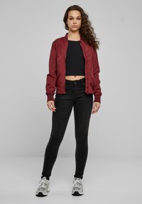 Blouson aviateur bordeaux, crop top noir, jean skinny noir et baskets grises. Texture lisse, coupe ajustée, poignets et ourlet côtelés.