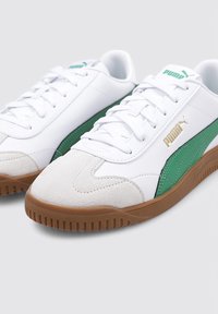 Zapatillas blancas con detalles en verde, puntera de ante y cordones blancos. Presentan una suela de goma texturizada y un logo dorado de la marca en el lateral.